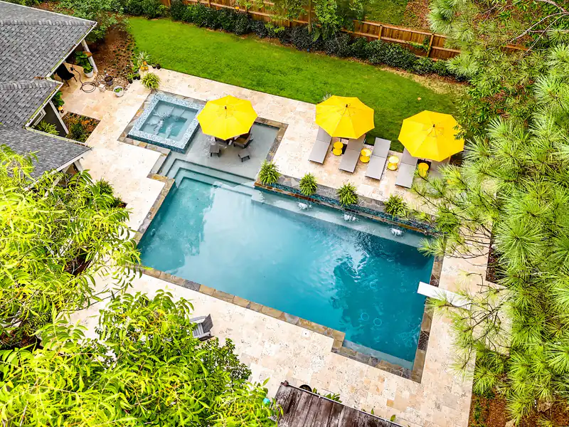 Aerial view of a rectangular pool with a tiled spa and yellow umbrellas