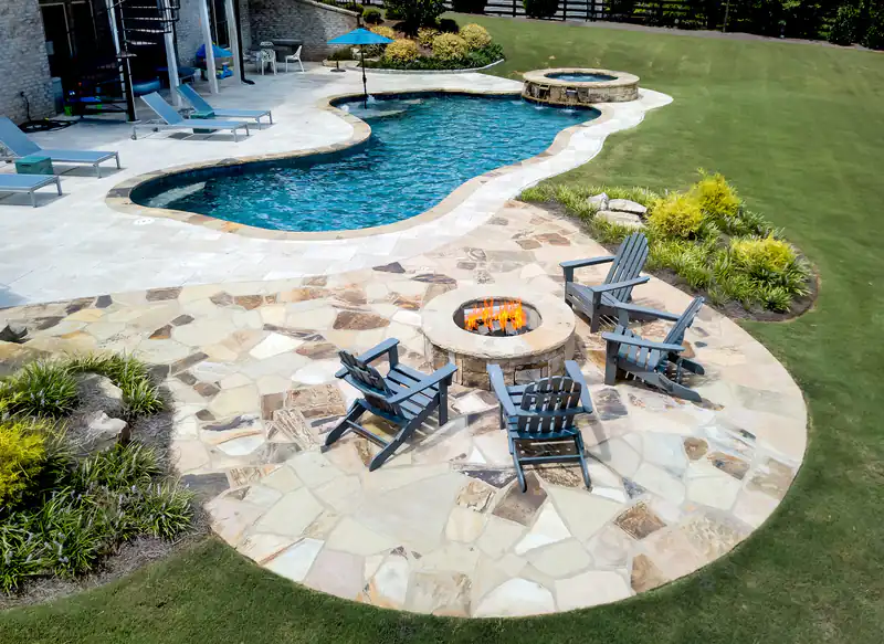 Aerial view of a freeform pool and spa beside a flagstone fire-pit circle with chairs