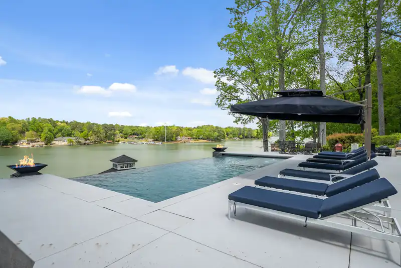 Infinity-edge pool above a lake with a black umbrella and lounge chairs