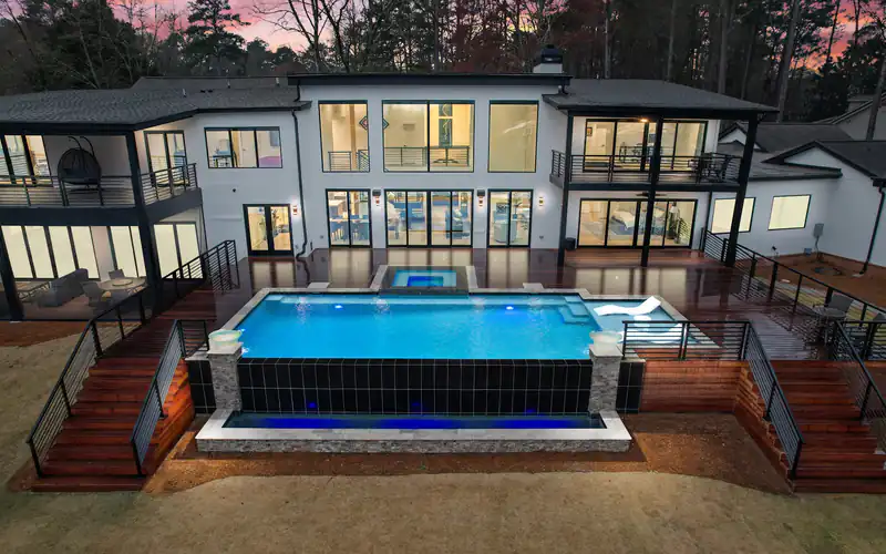 Vanishing-edge pool running the length of a glass and steel house at dusk