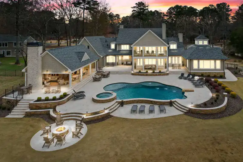 Lit pool at dusk below stone terraces and a fire pit on a hillside estate