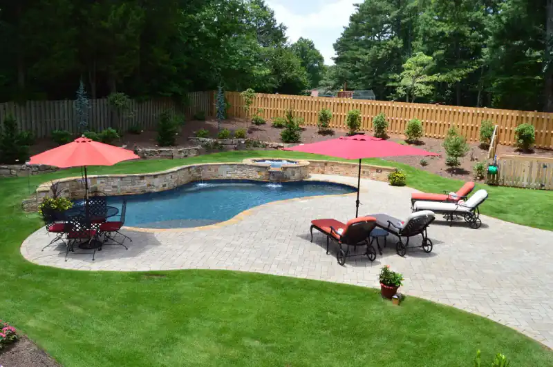A freeform pool with a raised stone wall, a red umbrella and a fenced yard